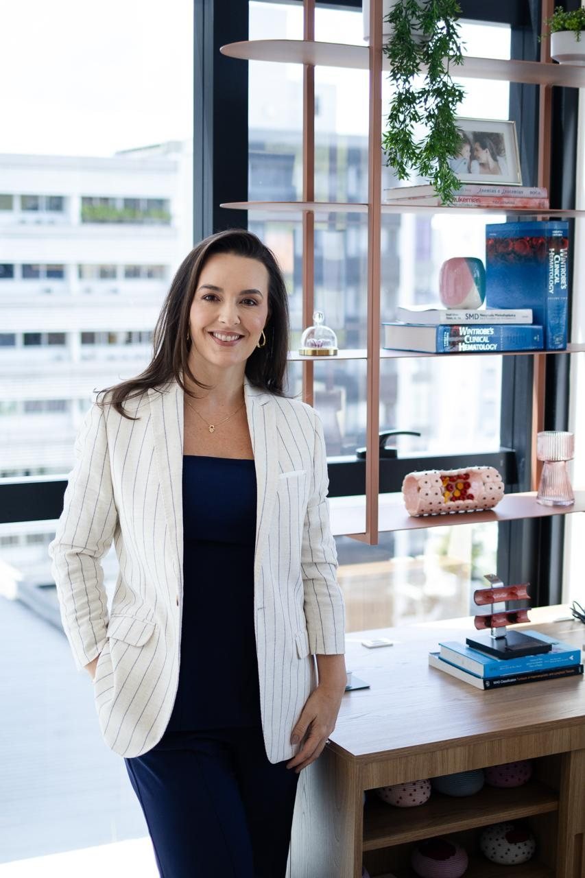 Dra. Andrezza Medina em seu consultório, com a biblioteca de hematologia
